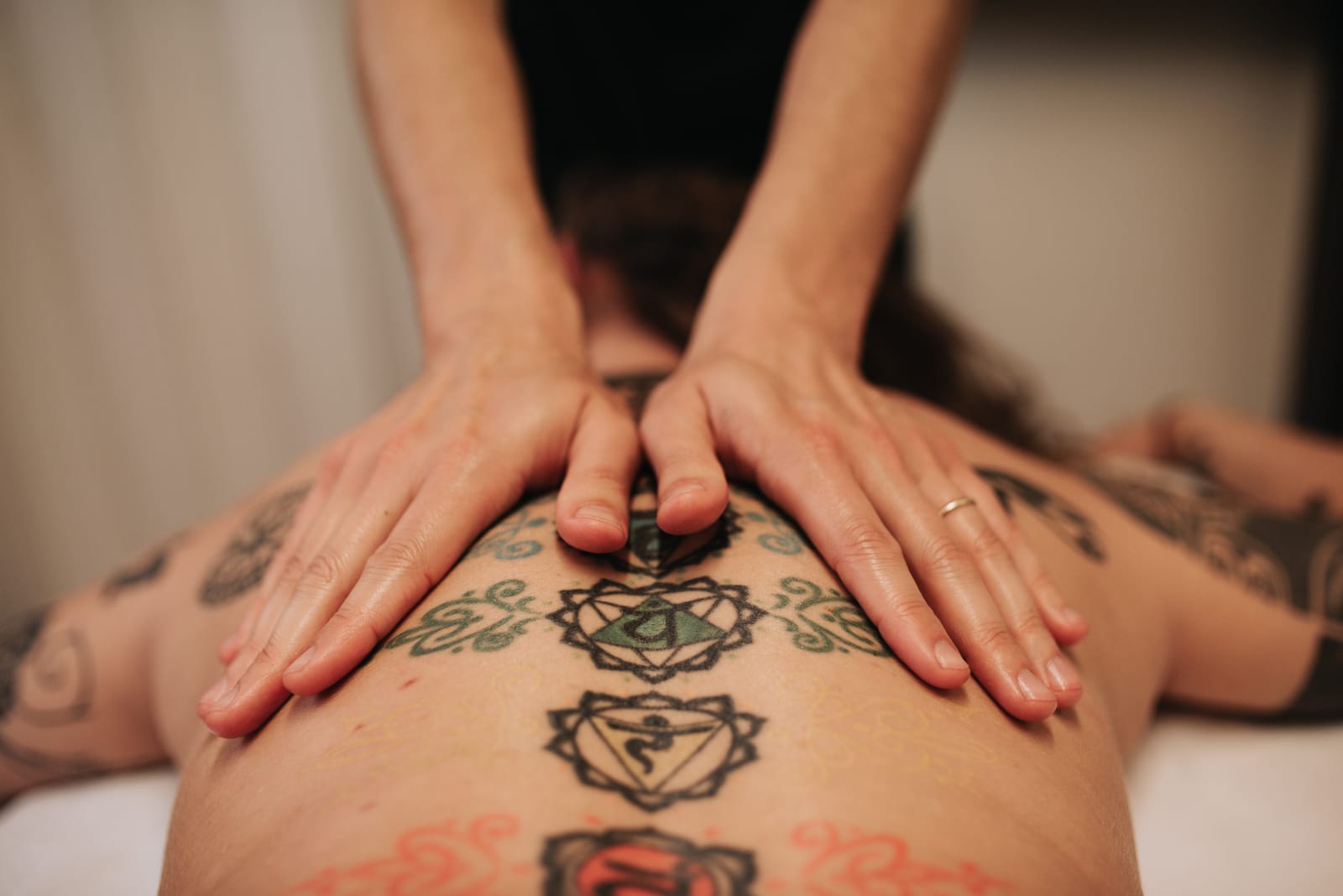 Mani appoggiate sulla schiena durante un trattamento Tao Veda, accanto ai simboli dei chakra tatuati lungo la colonna